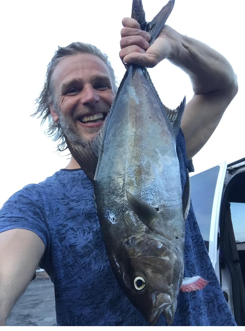 Hunter holds amberjack high on lava coast